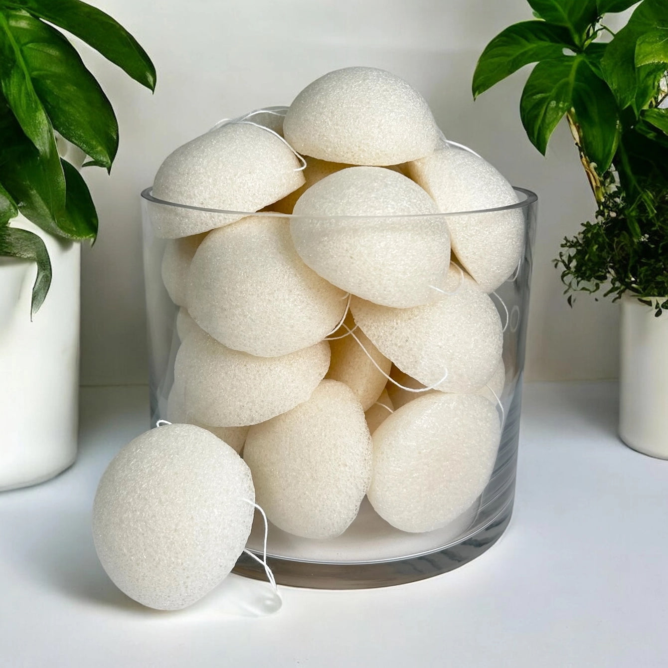 Glass container filled with konjac sponge polishing pearls on a light surface with plants in the background