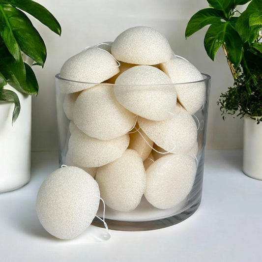 Glass container filled with konjac sponge polishing pearls on a light surface with plants in the background