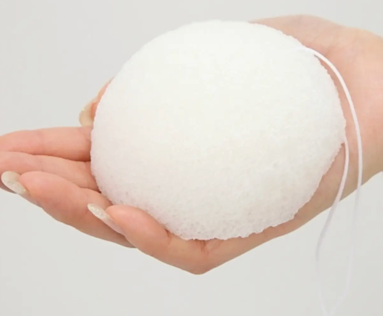 Hand holding a white konjac sponge polishing pearl against a light gray background