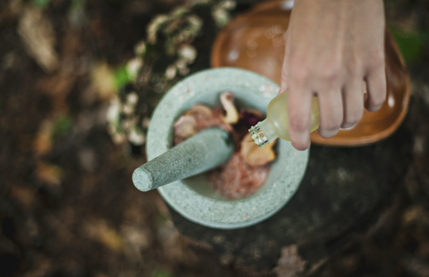 Photo of woman's hand pouring oil into mortar and pestle with rose petals.